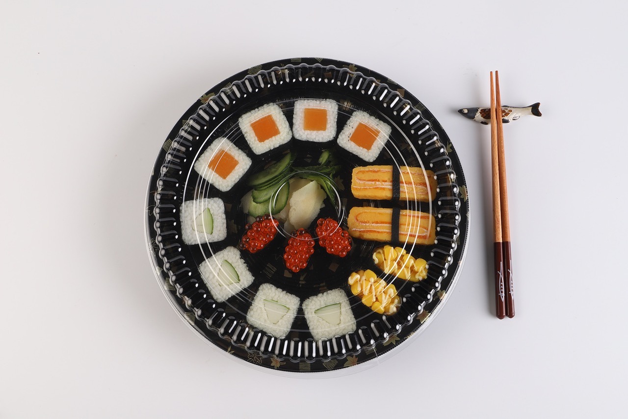 Top view of WL53 round black sushi container with clear lid and sushi arrangement
