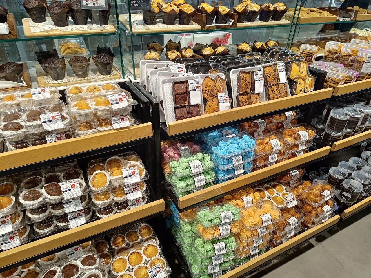 Is a Glass Food Container Better Than Plastic? Complete Guide 5 Clear plastic food packaging containers displaying muffins, cakes, cookies, and desserts in a retail bakery section.