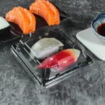 Black WL-0.1 sushi tray with clear lid holding two pieces of sushi