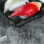 Detailed view of nigiri sushi inside a black WL-0.1 tray with clear cover