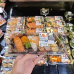 Clear-lid WL-01 sushi tray package held in front of a chilled display