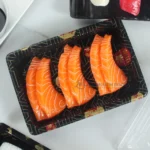 Black patterned WL-03 sushi tray displaying salmon sushi beside its clear fitted lid