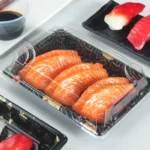 Close-up of salmon sushi inside a black patterned WL-03 box with clear fitted cover