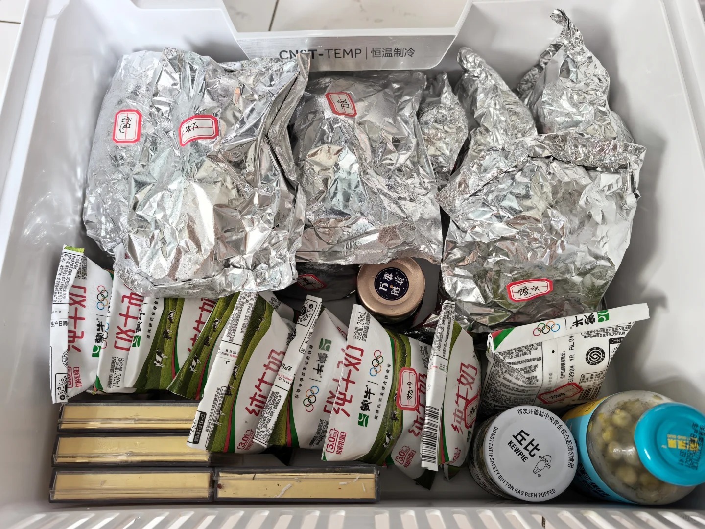 Aluminum foil wrapped food and dairy products stored inside a refrigerated cooler.